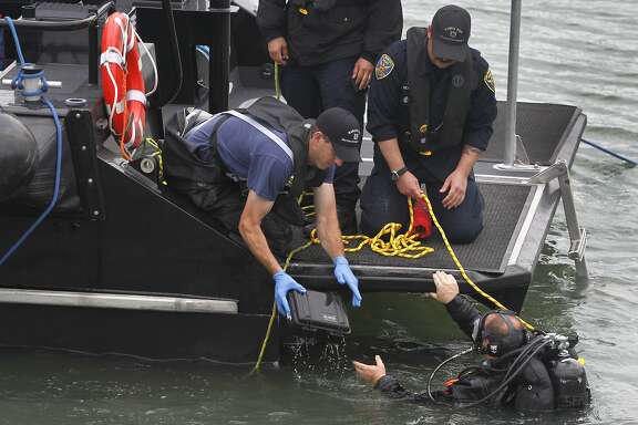 A police department diver hands a box possibly containing evidence found in the bay near Pier 14 to another officer in San Francisco, Calif. on Thursday, July 2, 2015 after a woman was shot and killed walking on the pier with her father yesterday afternoon.